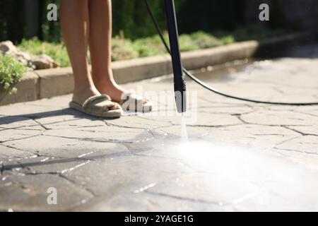 Nahaufnahme einer Frau, die den Gartenboden mit Wasser zu Hause mit Hochdruckreiniger reinigt Stockfoto