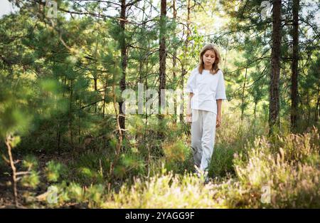 Ein kleines Kind spaziert ruhig auf einem Waldweg und genießt die Wärme der Sonne und die Ruhe der umliegenden Bäume und Pflanzen Stockfoto