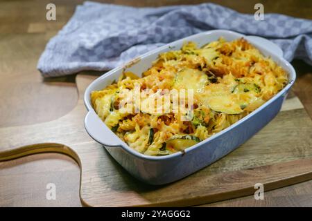 Gebackene Pasta mit Käse und Gemüse in einem blauen Auflauf mit Küchentuch auf einem rustikalen Holzbrett, hausgemachte Mahlzeit, ausgewählte Fokussierung, enge Tiefe Stockfoto