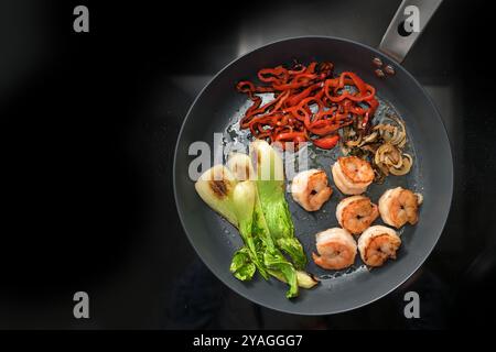 Bratpfanne mit gebratenen Garnelen und Gemüse wie Bok Choy, rote Paprika und Zwiebeln auf schwarzem Hintergrund, Kochen einer gesunden Mahlzeit, Low Carb Diät Stockfoto