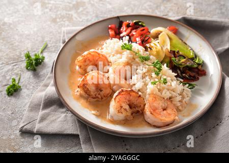 Gebratene Garnelen mit Krustentiersauce, Reis und Gemüse auf einem grauen Teller und beige Serviette auf einem Steingrund, kochen ein gesundes hausgemachtes Gericht, Kopie Stockfoto