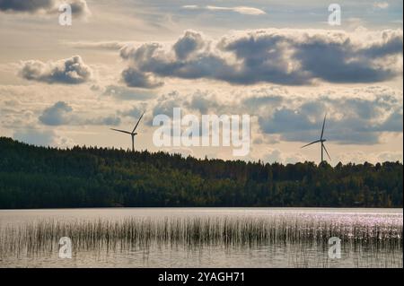 Windturbinen am Ufer eines Sees in Smaland, Schweden. Erneuerbare Energie vor Wolken und blauem Wasser. Natur aus Skandinavien Stockfoto