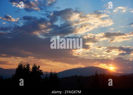 Ruhiger Abendhimmel mit blauen und weichen rosa Wolken bei Sonnenuntergang. Der Horizont leuchtet sanft und wirft Licht über Silhouetten von Kiefern und sanften Hügeln, wodurch eine friedliche und weitläufige Landschaft entsteht. Stockfoto