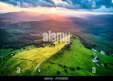 Blick aus der Vogelperspektive auf die atemberaubende ukrainische Landschaft bei Sonnenuntergang mit sanften grünen Hügeln, riesigen Wäldern und verstreuten Bauernhäusern. Warmes Licht umspült die Landschaft und schafft eine ruhige und malerische Atmosphäre. Stockfoto