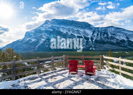 Rote adirondack-Stühle blicken an schneebedeckten, sonnigen Wintertagen über den Mount Rundle. Banff National Park wunderschöne Landschaft. Hoodoos Aussichtspunkt, Kanadische Rocky Mountains. Stockfoto