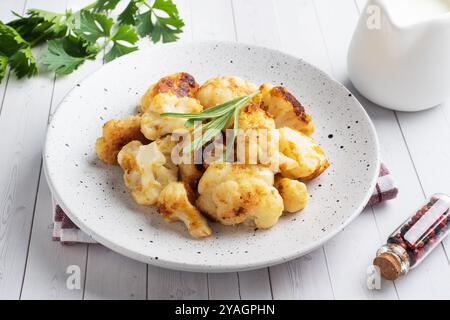 Gebratene Blumenkohlröschen im Teig auf einer weißen Platte. Weißer Holzhintergrund Stockfoto
