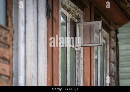 Öffnete ein kleines Fenster im alten Dorfhaus. Offenes verwittertes Fenster im Holzgebäude. Grunge-Hintergrund. Stockfoto