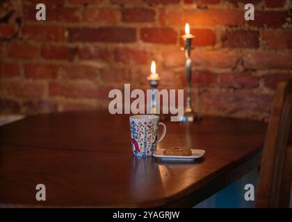Ein Gebäck und eine Tasse Kaffee auf einem Backsteinmauergrund. Morgens heißer Kaffee und Gebäck auf einem Holztisch bei Kerzenschein. Stockfoto