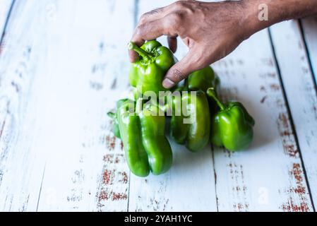 Mann pflückt frische grüne Paprika auf einer rustikalen weißen Oberfläche. Stockfoto