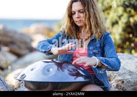 Schöne junge Frau, die fröhlich Handpfannentrommel am Meer spielt Stockfoto