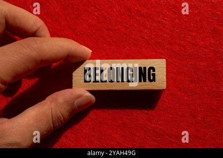 Zugehörige Nachricht auf Holzblock mit rotem Hintergrund. Konzeptionelles Zugehörigkeitssymbol. Kopierbereich. Stockfoto