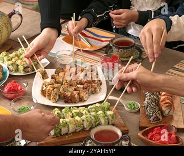 Sushi-Sets, Soße, Wasabi, Tee auf dem Feiertagstisch. Essen und traditionelle Gerichte der asiatischen Küche. Die Leute nehmen Brötchen mit Stäbchen. Tischeinstellung. Stockfoto