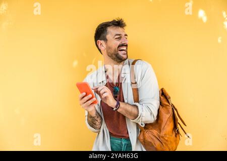 Junger modischer Hipster freiberuflicher Geschäftsmann posiert im Freien mit gelbem Wandhintergrund und Smartphone. Stil und Unabhängigkeit der Millennial männlichen Str. Stockfoto