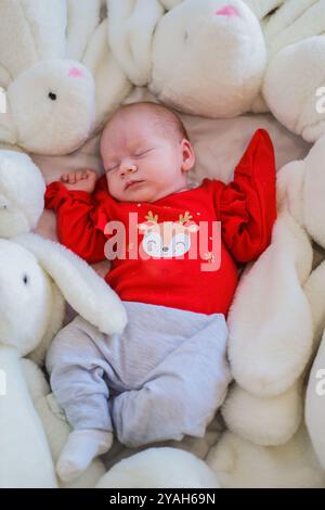 Schlafendes Kleinkind mit vielen Puppen Kaninchen auf weißer Decke Neugeborenes Konzept Stockfoto
