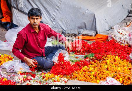 Ein lokaler Verkäufer hält Hibiskusgirlanden, die er auf dem Howrah Flower Market in der Strand Bank Road, Kalkutta, Westbengalen, Indien herstellt Stockfoto