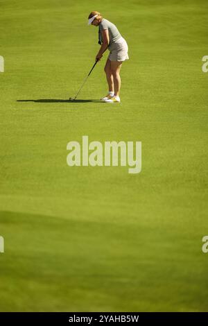 Eine Golferin konzentriert sich darauf, auf einem üppigen Golfplatz einen Fairway-Schuss zu machen, wobei sie Präzision und Konzentration in ihrer konkurrenzfähigen Golfkleidung zeigt. Stockfoto