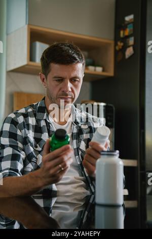 Der Mann sitzt am Tisch in der Küche und sieht sich verschiedene Flaschen mit Medikamenten-Kapseln an. Die Person nimmt Pillen oder Vitamine ein. Das Konzept der Nahrungsergänzungsmittel, medici Stockfoto