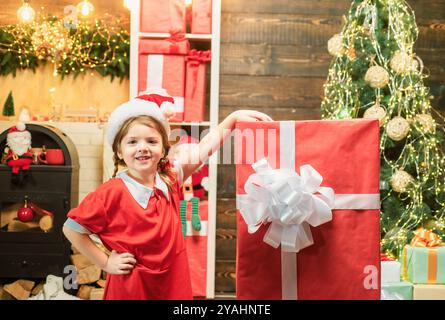 Glückliches Mädchen mit einer großen roten Geschenkbox. Junge, der sich in der Nähe des Weihnachtsbaums amüsiert. Winter Lieferservice für Kinder. Stockfoto