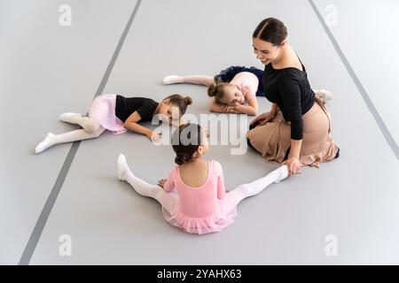 Frau unterrichtet Ballett für eine Gruppe von Studenten im Studio, die sich auf dem Boden dehnen Stockfoto