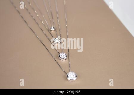 Sammlung von zarten Goldketten mit runden, mit Lünette besetzten Edelsteinanhängern, in absteigender Reihenfolge nach Größe auf beigefarbenem Hintergrund angeordnet Stockfoto