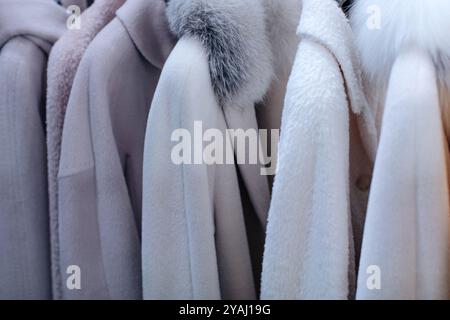 Weiße und graue Pelzmäntel für Frauen, die in einer Luxusboutique für Winterbekleidung nacheinander hängen Stockfoto