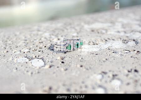 Das Bild zeigt einen eleganten Weißgoldring mit drei zentralen Smaragden, umgeben von kleinen Diamanten. Der Ring ist auf Marmor. Stockfoto