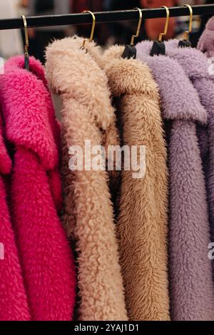 Luxuriöse Damenfellmäntel, rosa, beige, lila Winteroberbekleidung, die in einer Reihe an Kleiderbügeln auf einem Modemarkt hängt Stockfoto