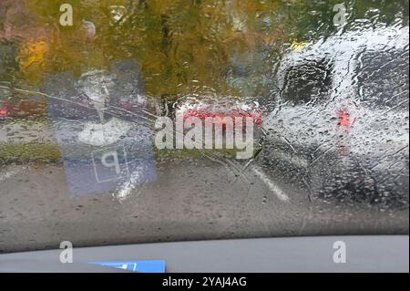 Das Foto zeigt eine regnerische Tagesszene, die durch eine Windschutzscheibe des Autos gesehen wird. Die Wassertropfen und -Streifen des Regens verzerren die Sicht nach draußen und machen es so Stockfoto