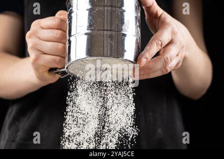 Der Koch siebt das Weizenmehl durch ein Metallsieb Stockfoto