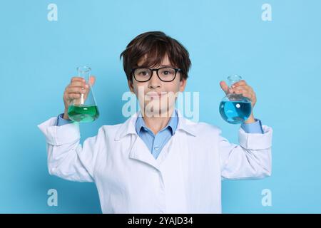 Junge mit Glaswaren, der vorgibt, Wissenschaftler zu sein, auf hellblauem Hintergrund. Träumen vom zukünftigen Beruf Stockfoto