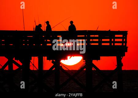 Isle Of Palms, Usa. Oktober 2024. Fisherman Silhouetten von einem dramatischen Sonnenaufgang werfen ihre Linien vor der Isle of Palms Pier am 14. Oktober 2024 in Isle of Palms, South Carolina. Klarer Himmel und warmes Wetter sind in der Prognose für das lowcountry. Quelle: Richard Ellis/Richard Ellis/Alamy Live News Stockfoto