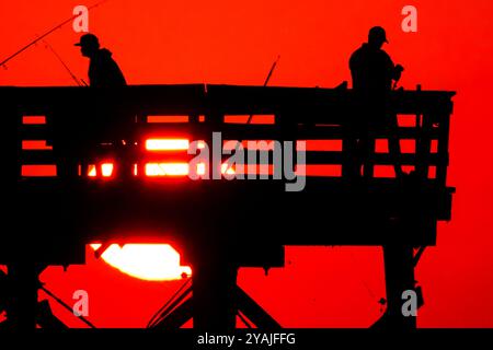 Isle Of Palms, Usa. Oktober 2024. Fisherman Silhouetten von einem dramatischen Sonnenaufgang werfen ihre Linien vor der Isle of Palms Pier am 14. Oktober 2024 in Isle of Palms, South Carolina. Klarer Himmel und warmes Wetter sind in der Prognose für das lowcountry. Quelle: Richard Ellis/Richard Ellis/Alamy Live News Stockfoto