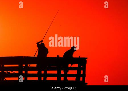 Isle Of Palms, Usa. Oktober 2024. Fisherman Silhouetten von einem dramatischen Sonnenaufgang werfen ihre Linien vor der Isle of Palms Pier am 14. Oktober 2024 in Isle of Palms, South Carolina. Klarer Himmel und warmes Wetter sind in der Prognose für das lowcountry. Quelle: Richard Ellis/Richard Ellis/Alamy Live News Stockfoto