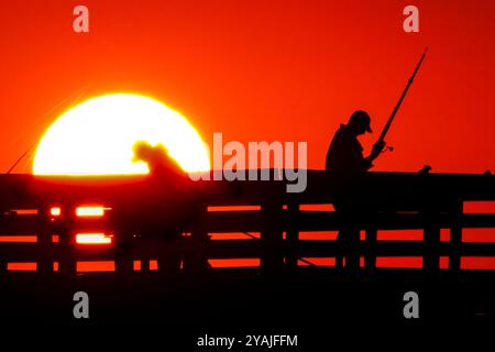 Isle Of Palms, Usa. Oktober 2024. Fisherman Silhouetten von einem dramatischen Sonnenaufgang werfen ihre Linien vor der Isle of Palms Pier am 14. Oktober 2024 in Isle of Palms, South Carolina. Klarer Himmel und warmes Wetter sind in der Prognose für das lowcountry. Quelle: Richard Ellis/Richard Ellis/Alamy Live News Stockfoto