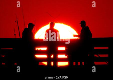 Isle Of Palms, Usa. Oktober 2024. Fisherman Silhouetten von einem dramatischen Sonnenaufgang werfen ihre Linien vor der Isle of Palms Pier am 14. Oktober 2024 in Isle of Palms, South Carolina. Klarer Himmel und warmes Wetter sind in der Prognose für das lowcountry. Quelle: Richard Ellis/Richard Ellis/Alamy Live News Stockfoto