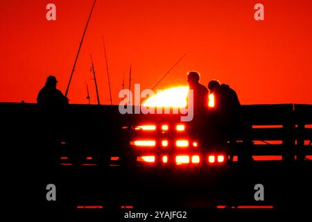 Isle Of Palms, Usa. Oktober 2024. Fisherman Silhouetten von einem dramatischen Sonnenaufgang werfen ihre Linien vor der Isle of Palms Pier am 14. Oktober 2024 in Isle of Palms, South Carolina. Klarer Himmel und warmes Wetter sind in der Prognose für das lowcountry. Quelle: Richard Ellis/Richard Ellis/Alamy Live News Stockfoto