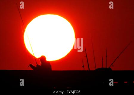 Isle Of Palms, Usa. Oktober 2024. Fisherman Silhouetten von einem dramatischen Sonnenaufgang werfen ihre Linien vor der Isle of Palms Pier am 14. Oktober 2024 in Isle of Palms, South Carolina. Klarer Himmel und warmes Wetter sind in der Prognose für das lowcountry. Quelle: Richard Ellis/Richard Ellis/Alamy Live News Stockfoto