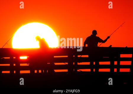 Isle Of Palms, Usa. Oktober 2024. Fisherman Silhouetten von einem dramatischen Sonnenaufgang werfen ihre Linien vor der Isle of Palms Pier am 14. Oktober 2024 in Isle of Palms, South Carolina. Klarer Himmel und warmes Wetter sind in der Prognose für das lowcountry. Quelle: Richard Ellis/Richard Ellis/Alamy Live News Stockfoto