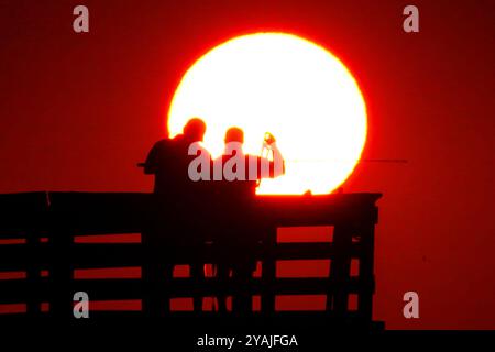 Isle Of Palms, Usa. Oktober 2024. Fisherman Silhouetten von einem dramatischen Sonnenaufgang werfen ihre Linien vor der Isle of Palms Pier am 14. Oktober 2024 in Isle of Palms, South Carolina. Klarer Himmel und warmes Wetter sind in der Prognose für das lowcountry. Quelle: Richard Ellis/Richard Ellis/Alamy Live News Stockfoto