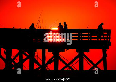 Isle Of Palms, Usa. Oktober 2024. Fisherman Silhouetten von einem dramatischen Sonnenaufgang werfen ihre Linien vor der Isle of Palms Pier am 14. Oktober 2024 in Isle of Palms, South Carolina. Klarer Himmel und warmes Wetter sind in der Prognose für das lowcountry. Quelle: Richard Ellis/Richard Ellis/Alamy Live News Stockfoto