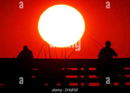 Isle Of Palms, Usa. Oktober 2024. Fisherman Silhouetten von einem dramatischen Sonnenaufgang werfen ihre Linien vor der Isle of Palms Pier am 14. Oktober 2024 in Isle of Palms, South Carolina. Klarer Himmel und warmes Wetter sind in der Prognose für das lowcountry. Quelle: Richard Ellis/Richard Ellis/Alamy Live News Stockfoto