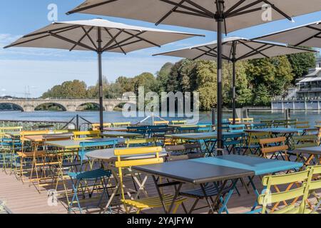 Stadtbild mit leeren Tischen und bunten Stühlen unter Sonnenschirmen im Restaurant über dem Ufer des Po, aufgenommen im hellen Herbstlicht in Turin, IT Stockfoto