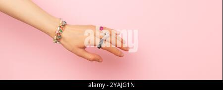 Banner mit handgefertigten Ringen und Armbändern auf einer weiblichen Hand vor rosa Hintergrund. Platz für Text. Stockfoto