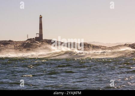 Silhouette des Leuchtturms am Diaz Point in Lüderitz, Namibia, bei Sonnenaufgang, mit einer Welle im Vordergrund. Stockfoto
