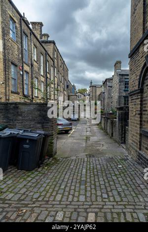 Eine Gasse (Ginnel, snicket, Passage, Backstreet) zwischen Reihen von Reihenhäusern (Wohnhäusern) in der Weltkulturerbestätte Saltaire, Yorkshire. Stockfoto