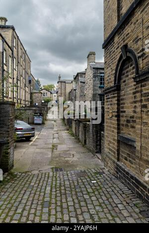 Eine Gasse (Ginnel, snicket, Passage, Backstreet) zwischen Reihen von Reihenhäusern (Wohnhäusern) in der Weltkulturerbestätte Saltaire, Yorkshire. Stockfoto