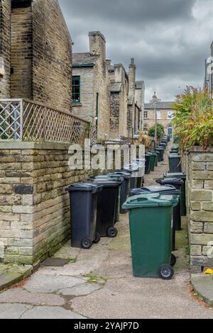 Wheelie-Mülltonnen säumen den Ginnel (Galleyway, snicket) zwischen zwei Reihen von Terrassenhäusern (ehemalige Salzmühle Workers Housing) in Saltaire, Yorkshire. Stockfoto