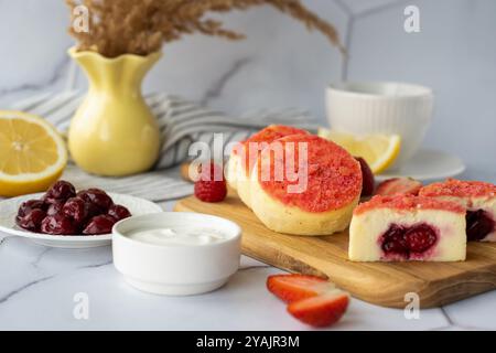 Köstlicher Käsekuchen mit Kirschfüllung und frischen Beeren, serviert mit Sauerrahm und Kaffee in einer gemütlichen Küche. Stockfoto