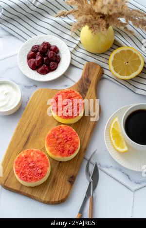Mini-Käsekuchen mit Kirschfüllung und Erdbeerbelag auf einem Holzbrett, serviert mit Kaffee Stockfoto