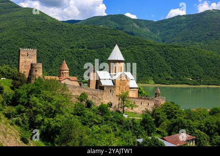 Landschaft zwei Kirchen und quadratischer Turm der ananuri Festung hinter einer befestigten Mauer mit Blick auf das grüne Wasser des Zhinvali See und bewaldete Hügel Stockfoto